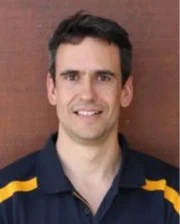 Portrait of Dr. Albert Solé Guitart in a dark polo shirt with yellow accents standing in front of a reddish-brown background.