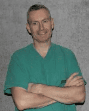 Dr. Casper Lindegaard smiling, wearing green medical scrubs, standing with arms crossed.