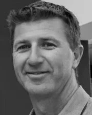 Black and white headshot of a middle-aged man with short hair smiling at the camera.