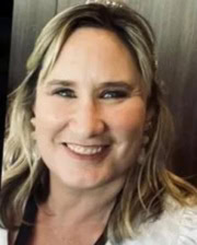 Close-up headshot of Dr. Holly Lewis smiling with shoulder-length blonde hair and a dark background.