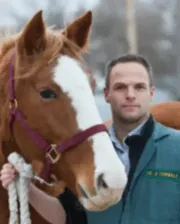 Dr. James Carmalt standing beside a chestnut horse with a white blaze, wearing a maroon halter.