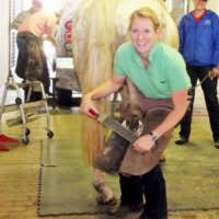 Dr. Jen Lugton trimming a horse's hoof in a veterinary facility with other professionals in the background.