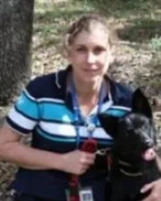 Dr. Jo Rainger outdoors with a black dog, wearing a striped polo shirt and holding a red leash.