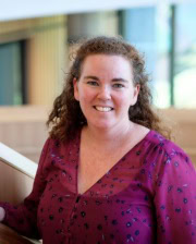 Dr. Laura Hardefeldt smiling and standing indoors, wearing a purple blouse with a softly blurred background.