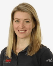 Dr. Laura Quiney smiling, with straight blonde hair, wearing a dark polo shirt with embroidered logos.