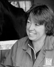 Dr. Leanne Begg smiling in a barn setting, wearing a veterinary jacket with a horse visible in the background.