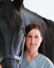 Dr. Natasha Werpy smiling, wearing scrubs, standing beside a black horse.