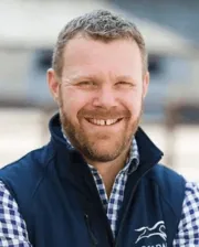 Dr. Tim Barnett smiling, wearing a navy vest over a blue and white checkered shirt.