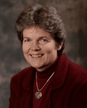 Professional headshot of Dr. Amy Grice wearing a burgundy jacket and necklace, smiling against a blurred studio background.