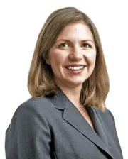 Professional portrait of a smiling woman in a gray blazer against a white background.