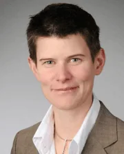 Professional headshot of Dr. Astrid Bienert-Zeit wearing a tan blazer and white shirt, smiling against a neutral background.