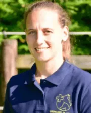Dr. Elke Pollaris smiling, wearing a navy polo shirt with an embroidered equine logo, standing outdoors.