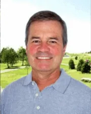 Dr. Scott Marx smiling outdoors, wearing a light blue polo shirt, with a scenic green landscape in the background.