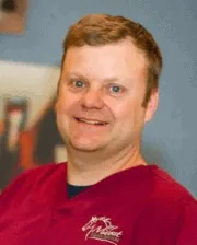 Professional photo of Dr. Travis Henry wearing a burgundy Midwest Veterinary Dental Services scrub top, smiling indoors.