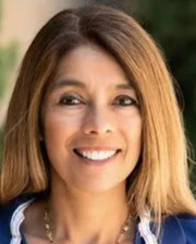 Headshot of Dr. Monica Aleman smiling outdoors, wearing a navy jacket with long brown hair.