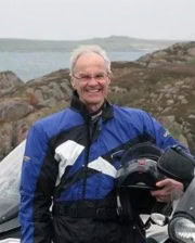 Prof. Derek Knottenbelt smiling in a blue motorcycle jacket while holding a helmet in a scenic outdoor setting.