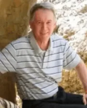 Professor Gary Wilson smiling, wearing a light grey and white striped polo shirt, seated outdoors.