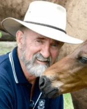 Professor Chris Pollitt smiling, wearing a wide-brim hat, next to a brown horse.