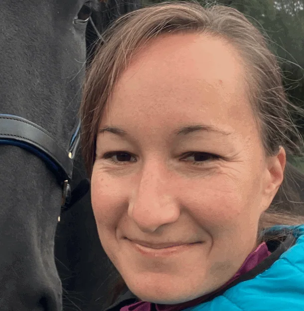 Close-up of Dr. Varadi Anna smiling next to a dark horse wearing a bridle.