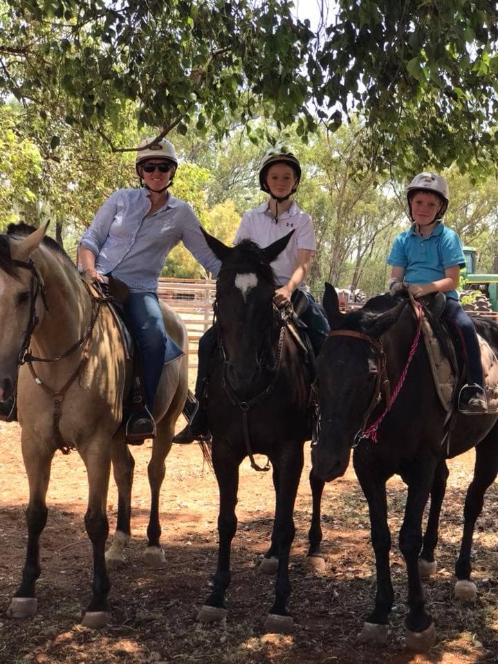 Dr. Olivia and two young boys sitting on horseback under shaded trees on a sunny day