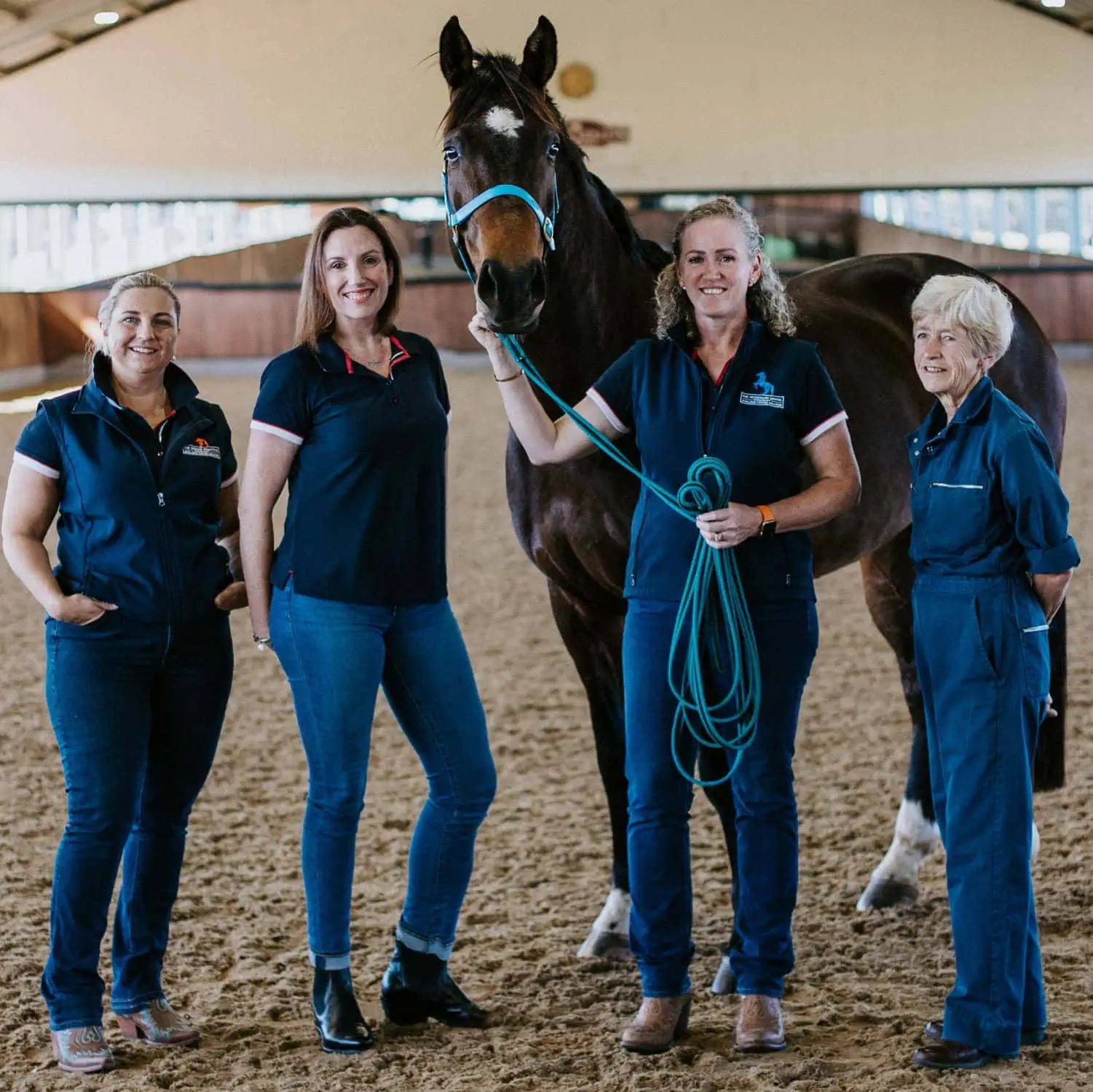 Four women from The Equine Practice Company standing with a horse in an indoor arena