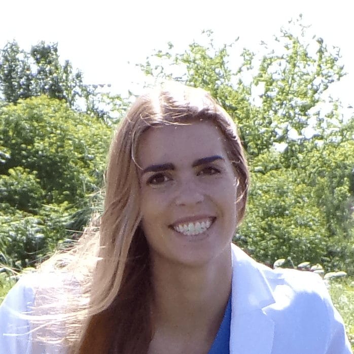 Dr. Abbey Floyd smiling outdoors in a white coat with trees in the background.
