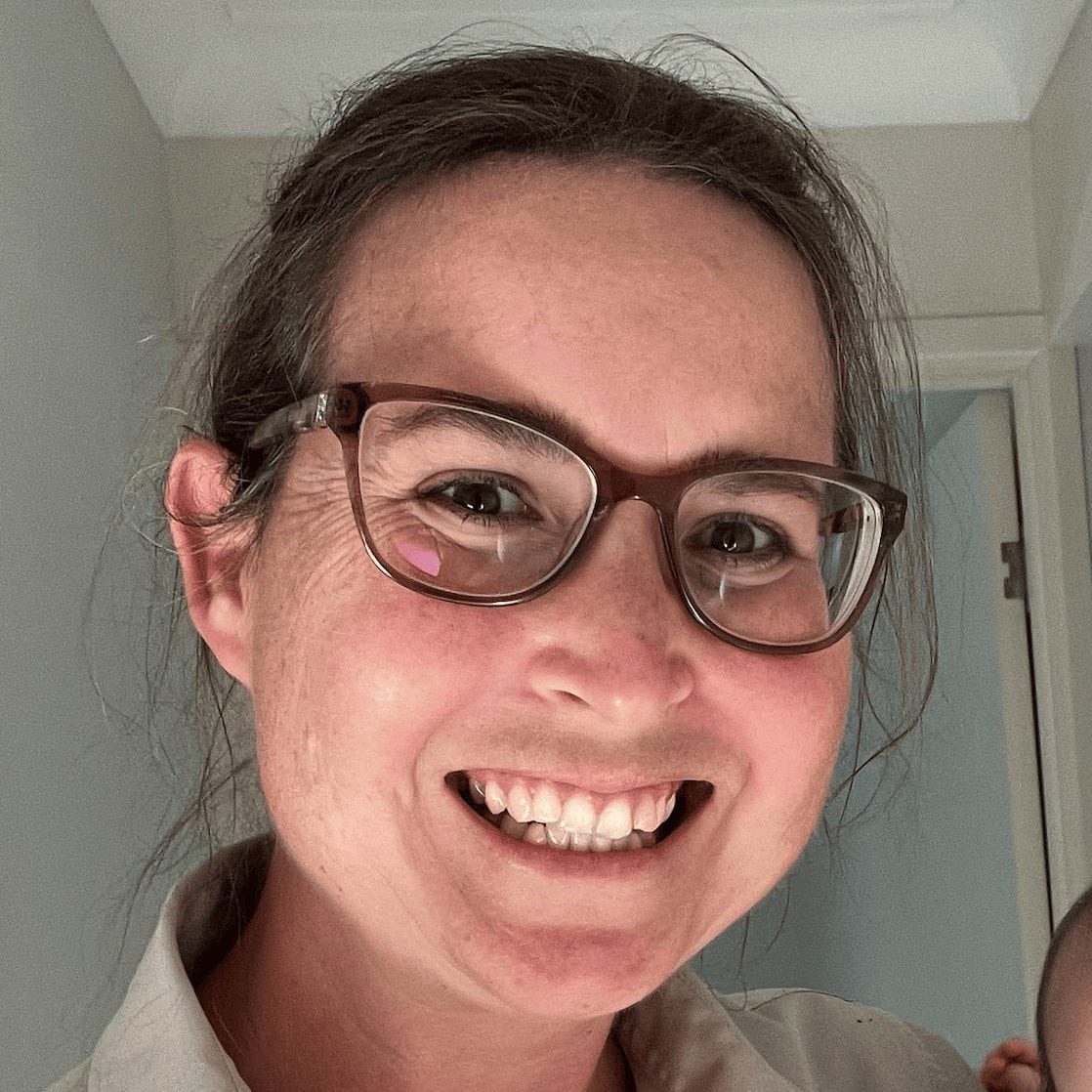 Dr. Rachel Kent smiling indoors while wearing glasses and a collared shirt.