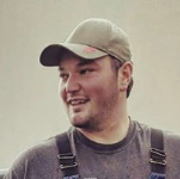 Jacob Murphy wearing a baseball cap and dark suspenders, smiling and looking to the side.
