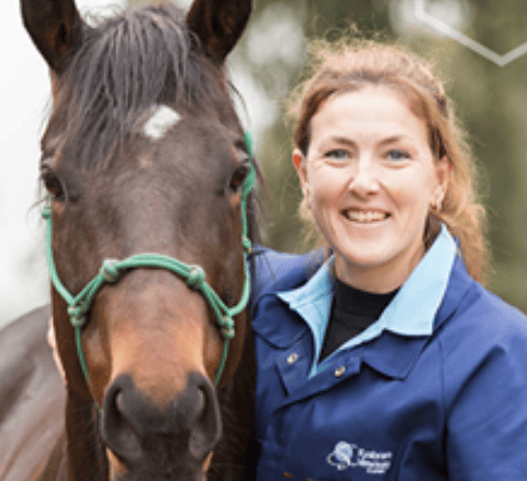 Veterinarian Clare Williams-Paterson smiling beside a brown horse wearing a green halter.