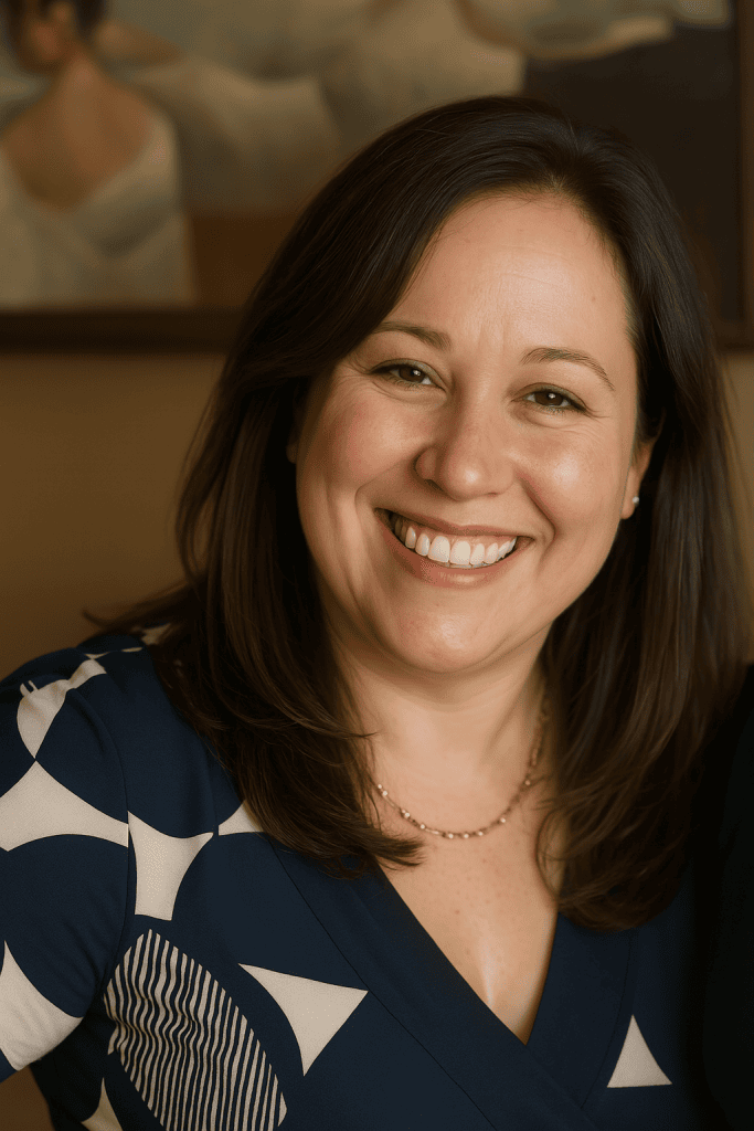 Zoe Morris smiling in a navy blue patterned blouse with a blurred painting in the background.